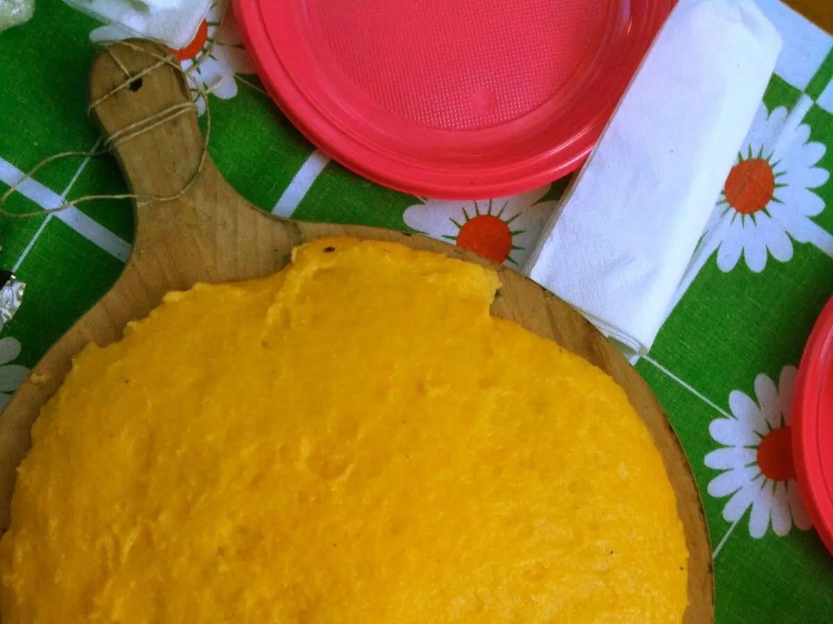 Polenta cremosa amarilla en una fuente de madera sobre un mantel verde de margaritas