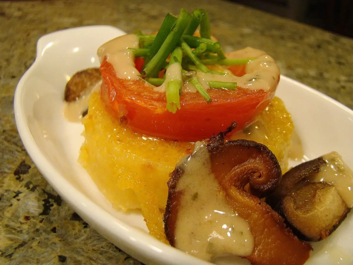 Polenta con tomate asado y setas shiitake salteadas en una fuente blanca con espárragos por encima