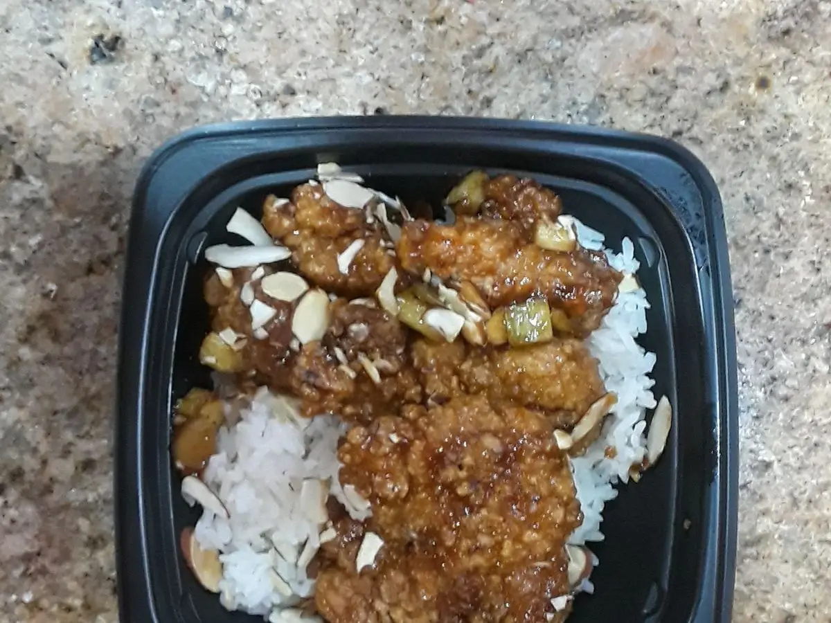 Pollo salteado con láminas de almendra sobre arroz blanco en un recipiente negro