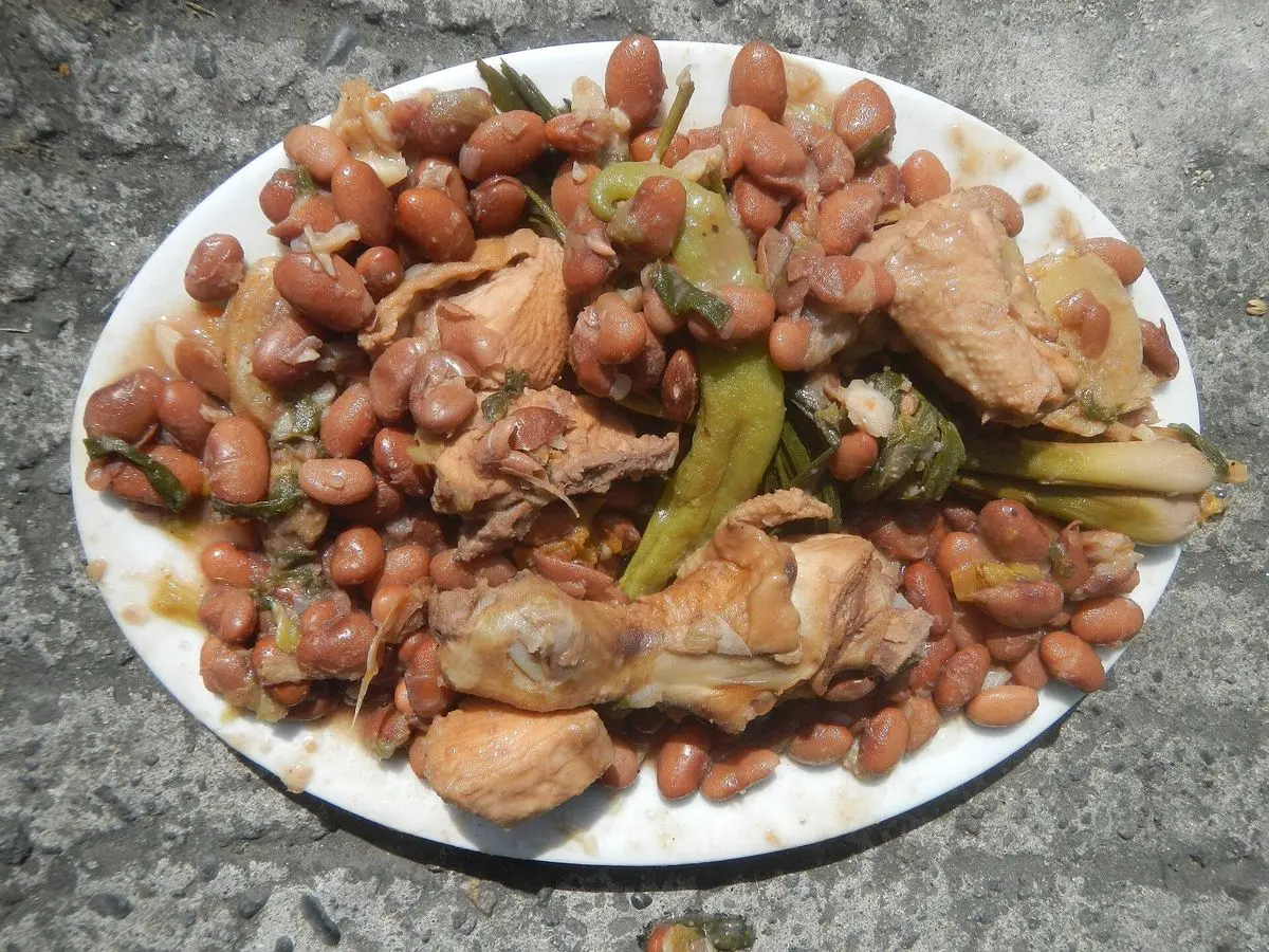 Plato blanco con guiso de alubias pintas y trozos de pollo con vainas verdes