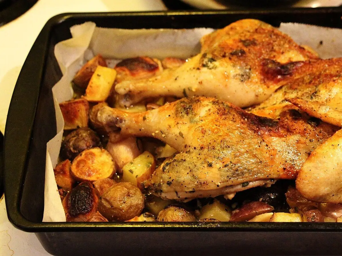 Pollo asado troceado sobre patatas doradas en una bandeja de horno