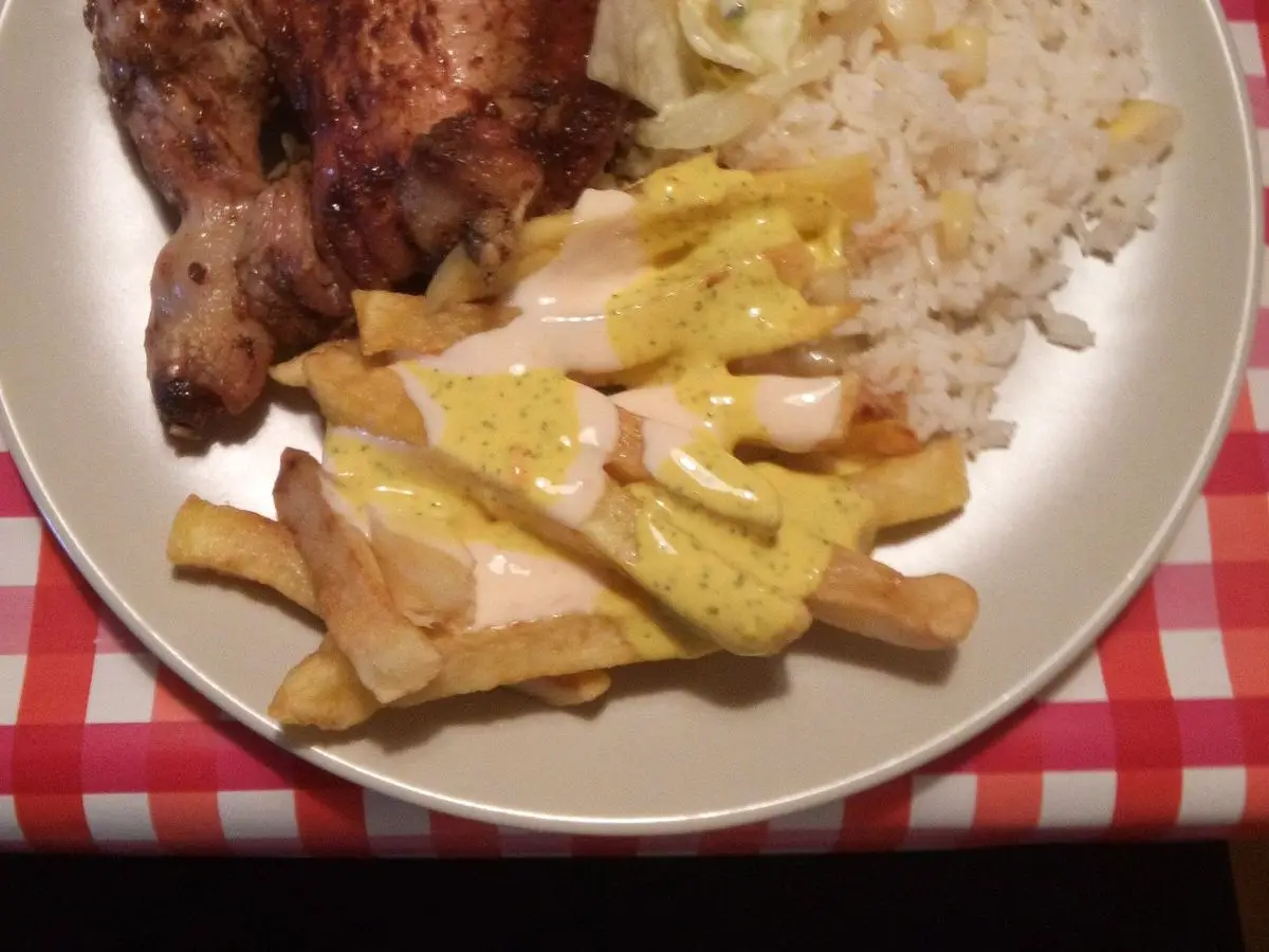 Cuarto de pollo a la brasa con arroz blanco, patatas fritas y ensalada en un plato sobre mantel de cuadros