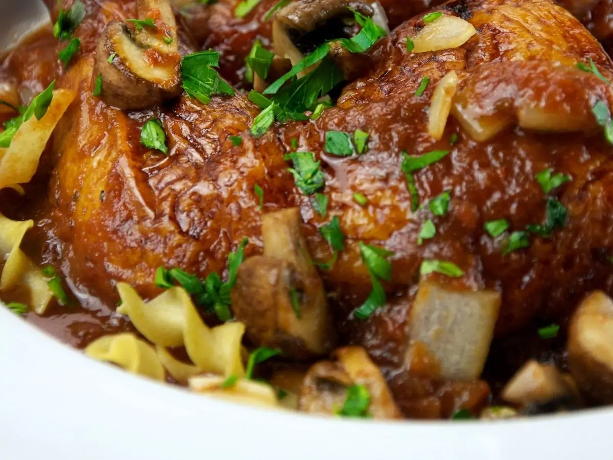 Muslo de pollo guisado con champiñones, cebolla y salsa de tomate sobre pasta