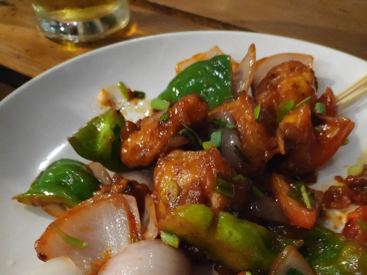 Pollo salteado en salsa picante con pimiento verde, cebolla y cebolleta en un plato blanco