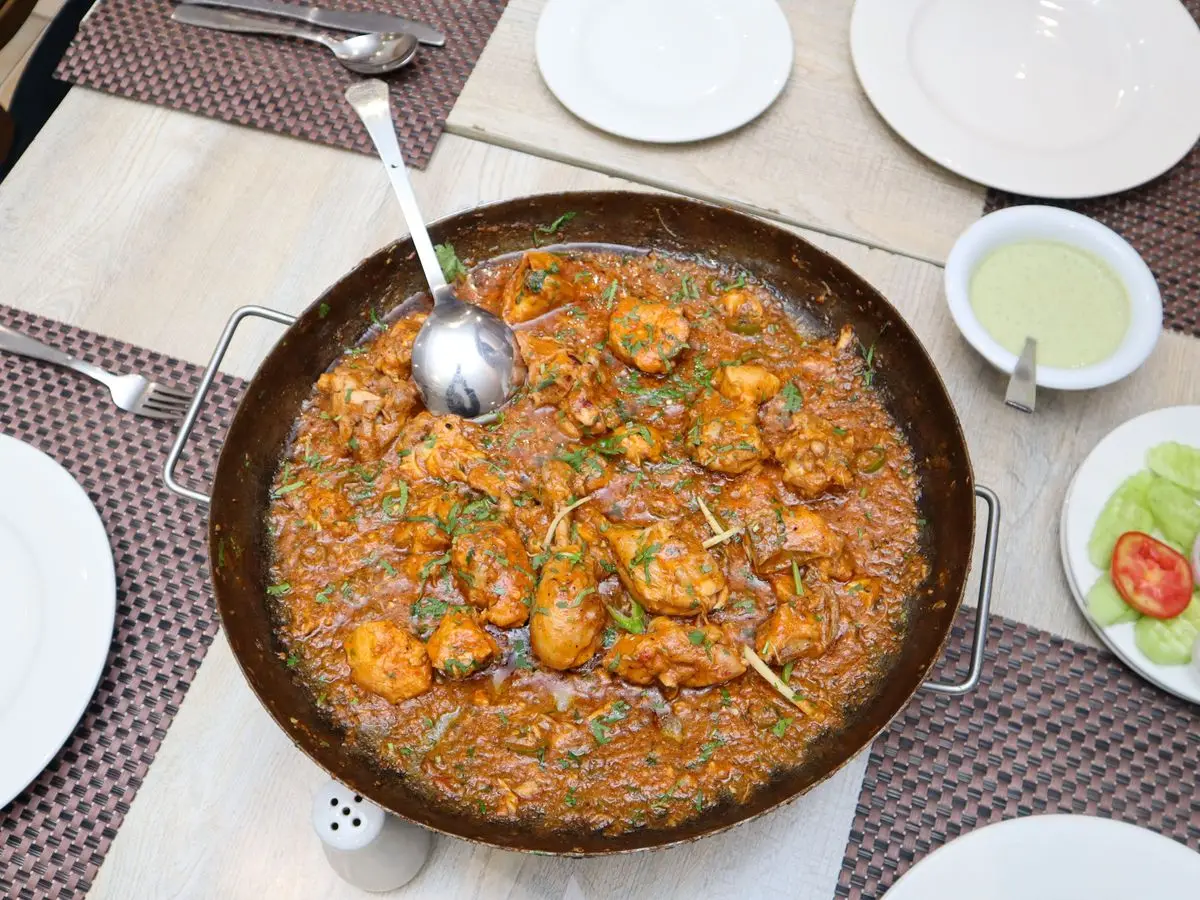 Cazuela grande de pollo guisado en una salsa roja de tomate y especias, con un cazo