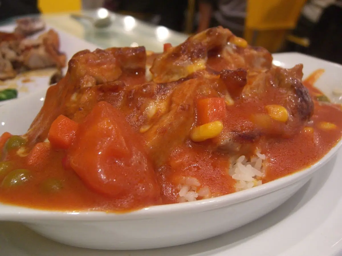 Pollo en salsa de tomate con trozos de tomate sobre arroz blanco en un plato