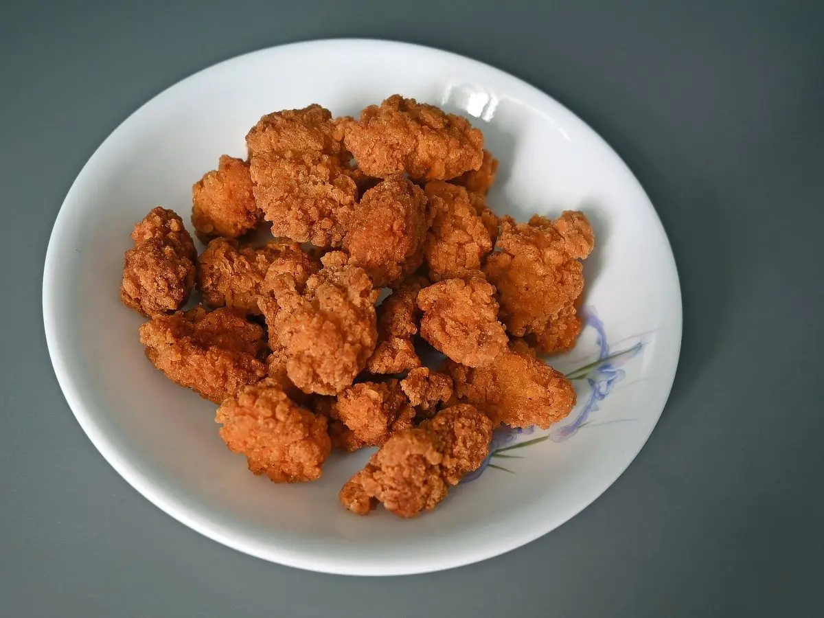 Plato blanco con trozos de pollo frito crujiente y especiado, estilo taiwanés, sobre una mesa gris