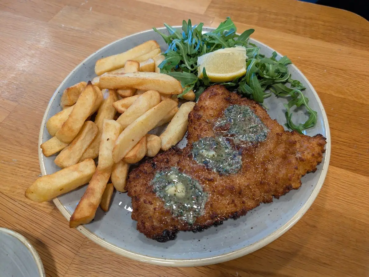 Escalope de pollo empanado con patatas fritas, rúcula y cuña de limón en un plato