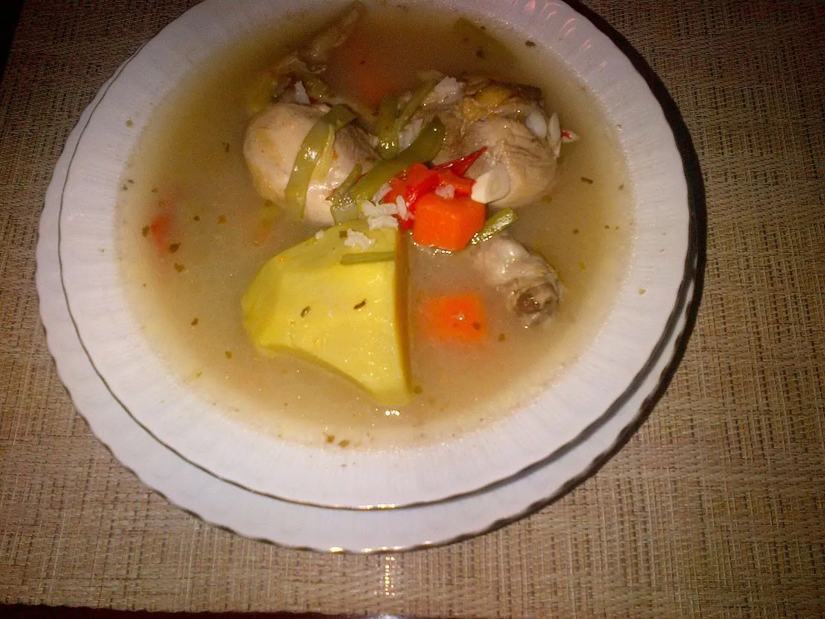 Plato hondo de caldo de pollo con muslos, patata y zanahoria en un guiso de color amarillento