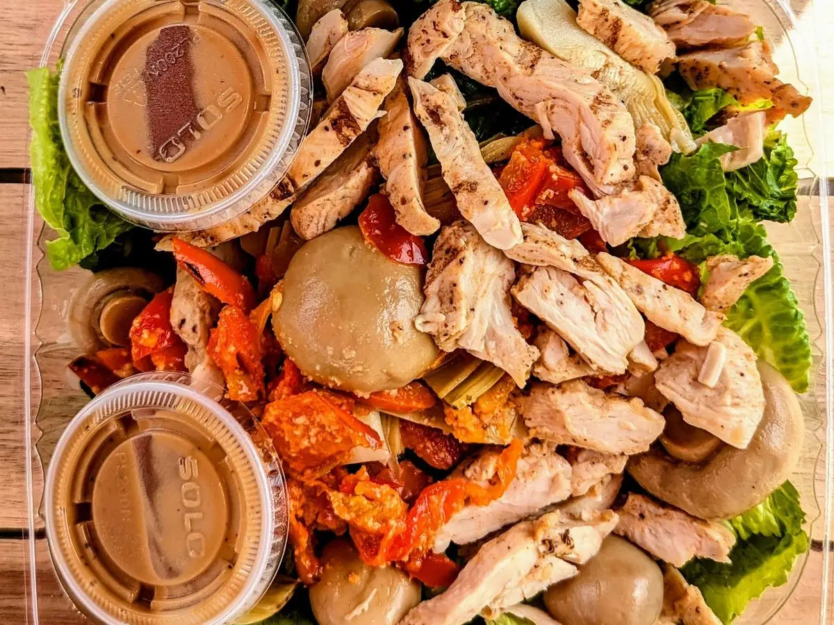 Ensalada con tiras de pollo, champiñones en escabeche y pimiento sobre hojas verdes con dos salsas