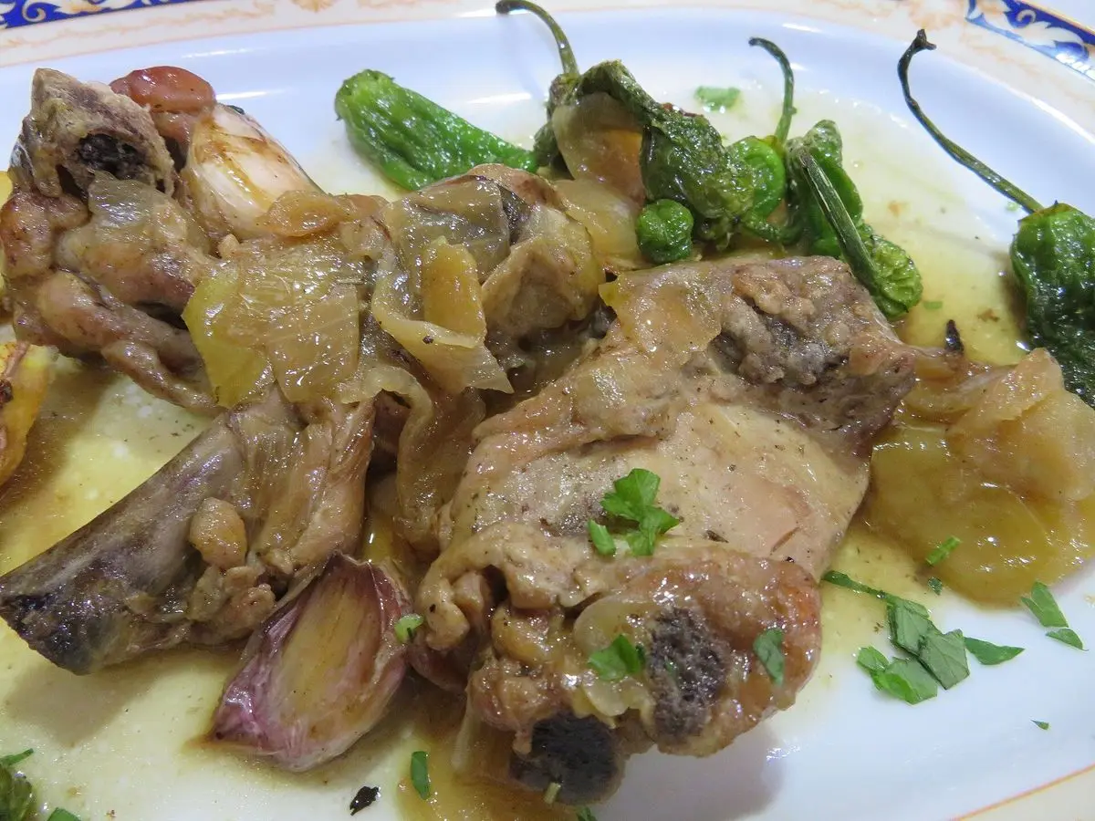 Plato de pollo guisado en trozos con cebolla pochada, pimientos verdes y perejil