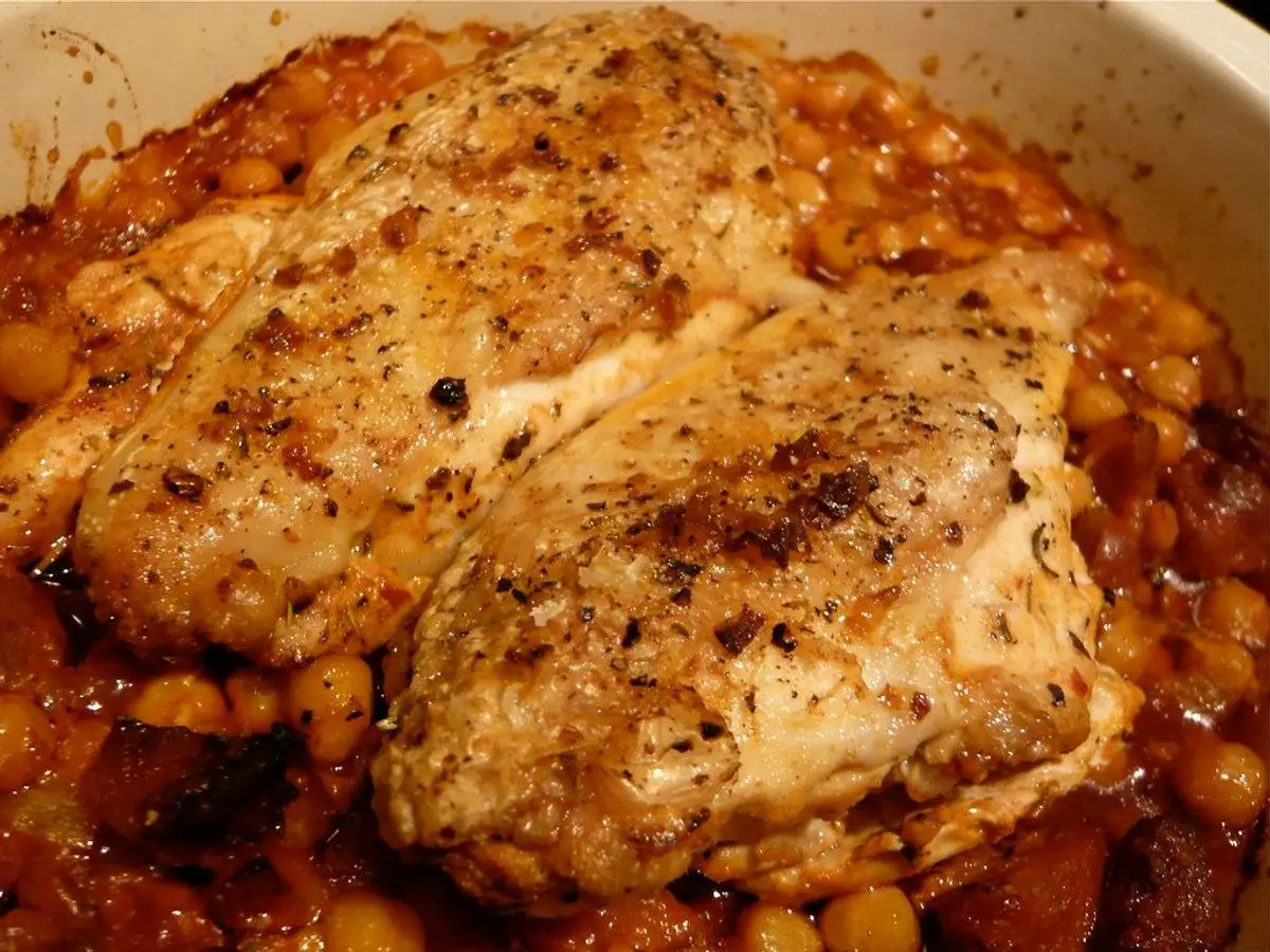 Pollo guisado sobre un lecho de garbanzos y salsa de tomate en una cazuela