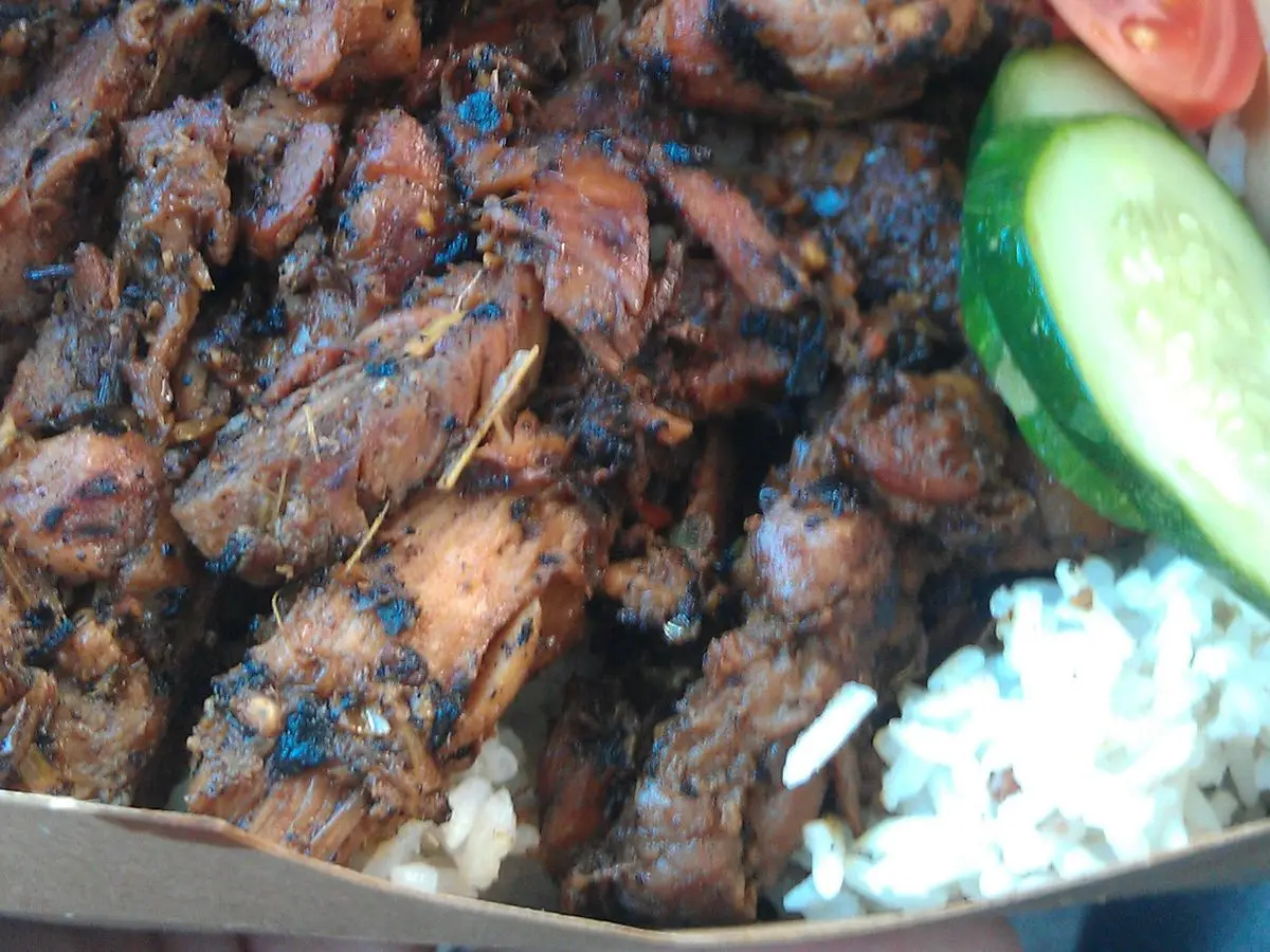 Trozos de pollo a la brasa glaseado en una caja con rodaja de tomate y pepino