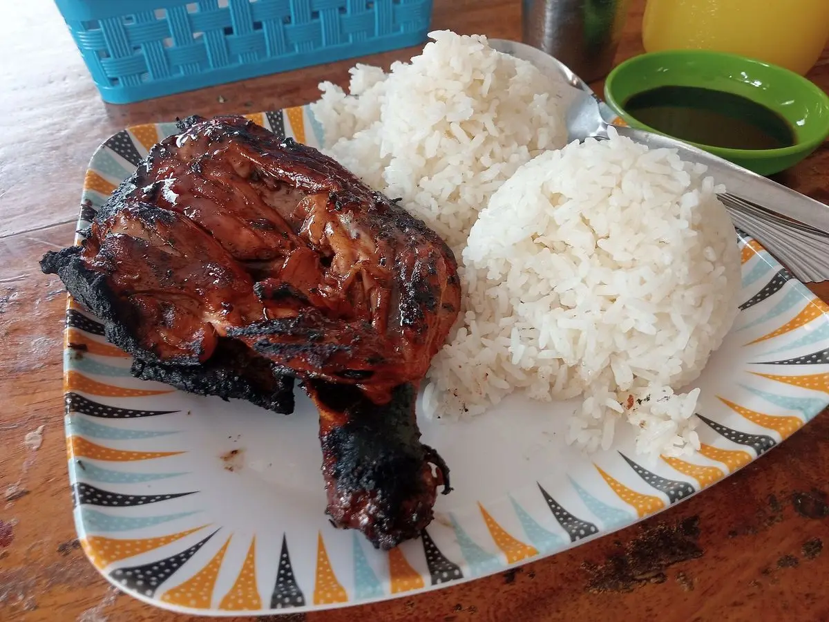 Pollo inasal asado a la brasa con arroz blanco y cuencos de salsas y lima sobre una mesa de madera