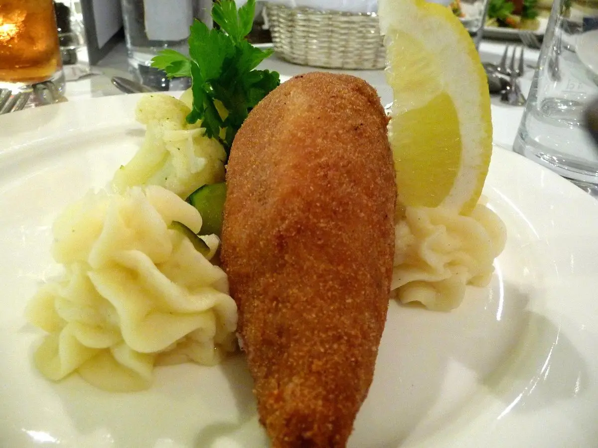 Pollo empanado relleno con puré de patata, perejil y rodaja de limón en un plato blanco