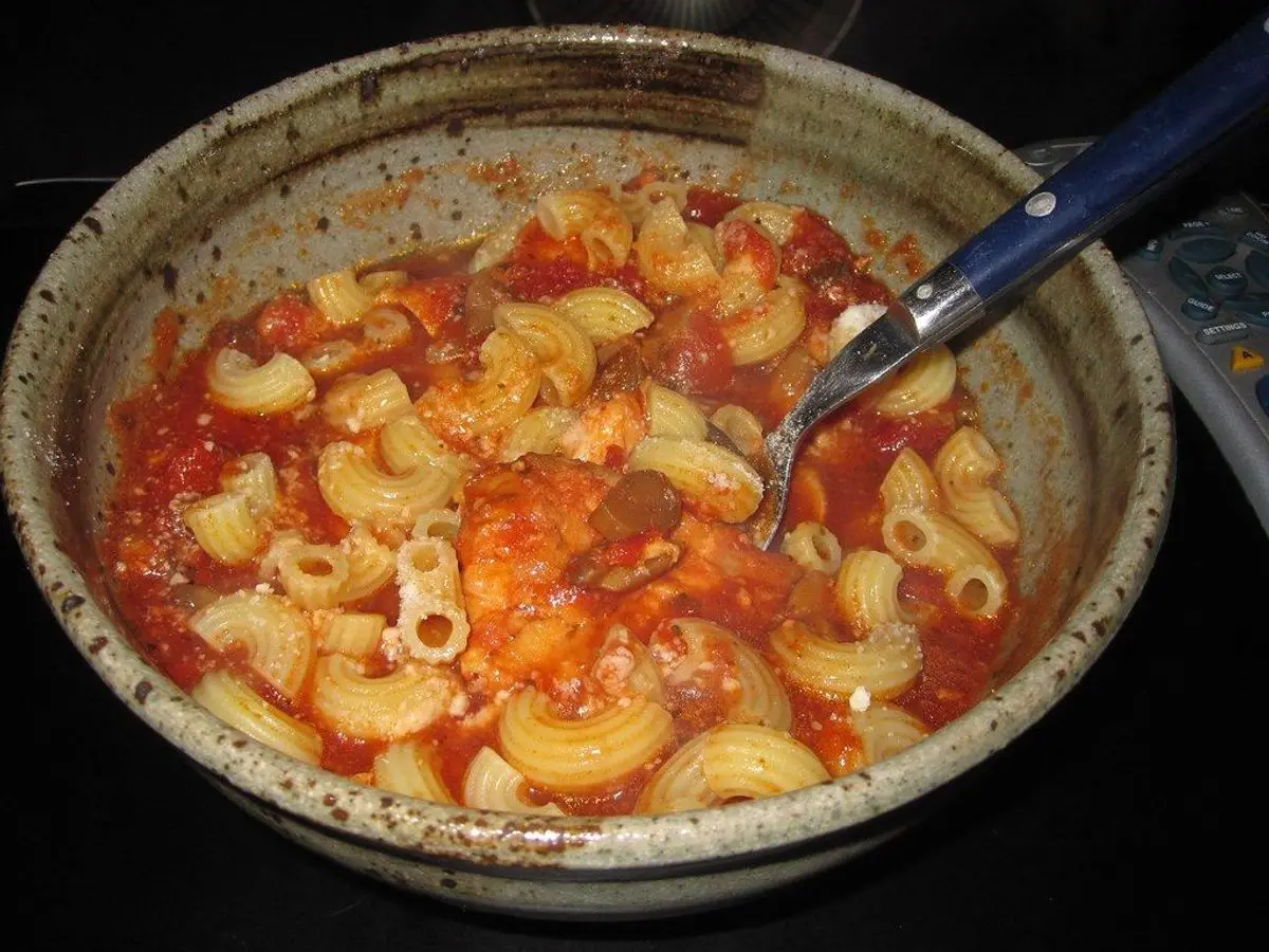 Cuenco de pasta corta con pollo en salsa de tomate roja y una cuchara