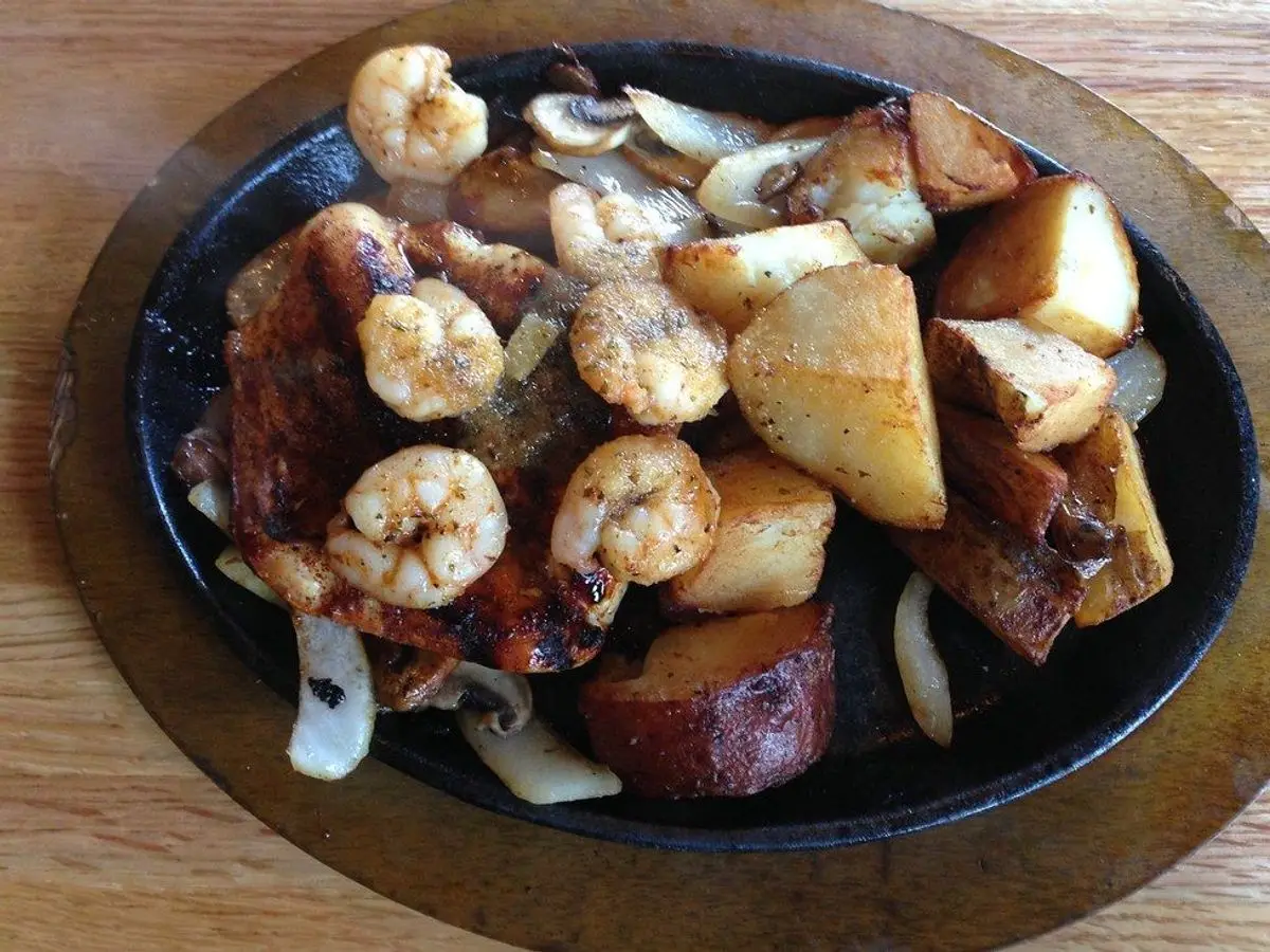 Plancha de hierro con pollo, gambas, patata y champiñones salteados con cebolla