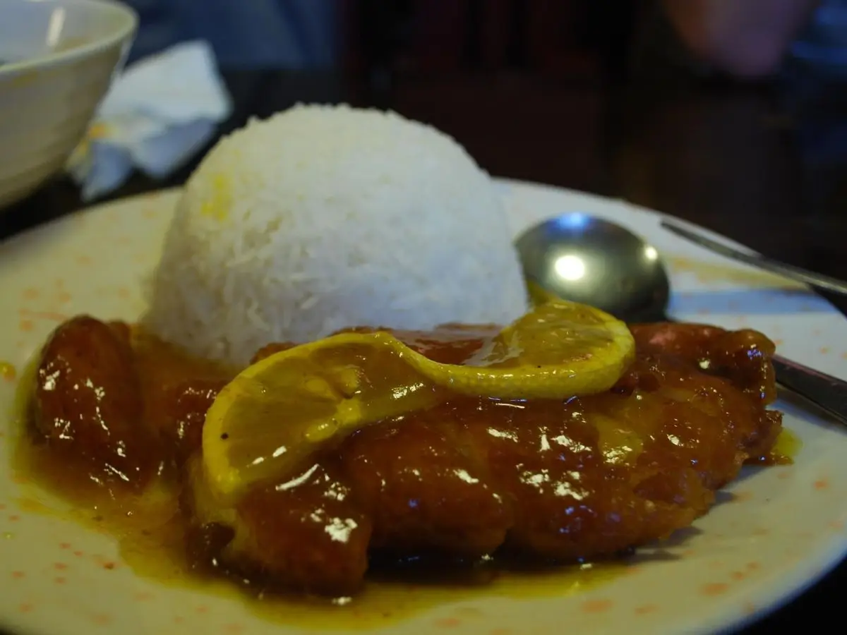 Pollo al limón glaseado con rodajas de limón y una bola de arroz blanco en un plato