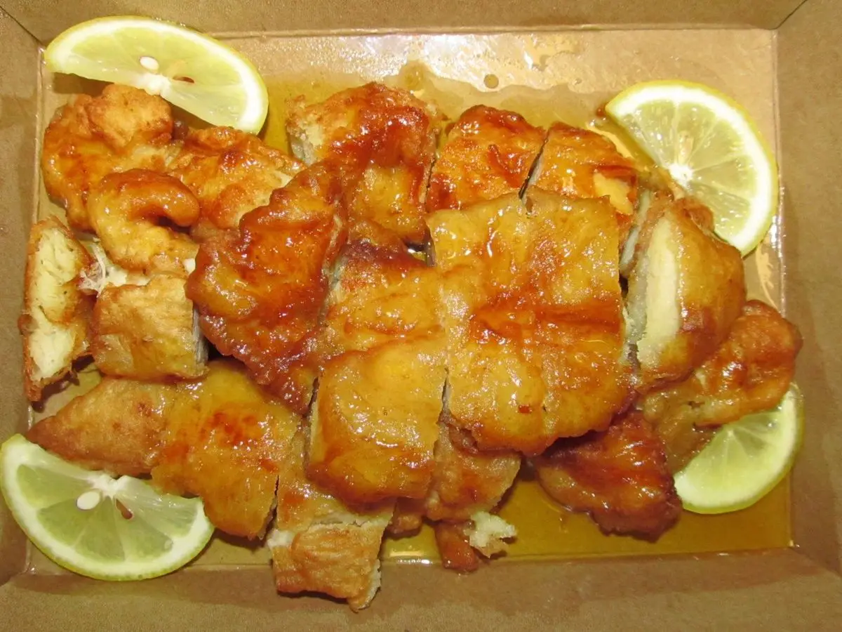 Trozos de pollo dorado glaseado con rodajas de limón en una caja de cartón
