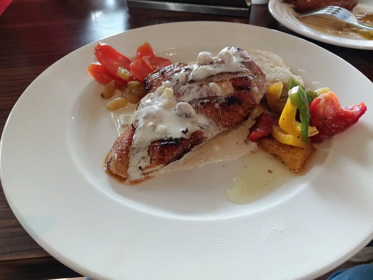 Pechuga de pollo a la plancha con salsa blanca cremosa y pimientos de colores en un plato blanco