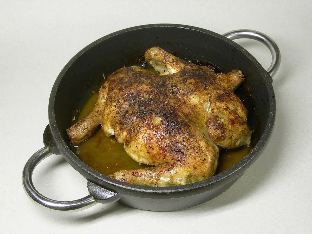 Pollo aplastado asado y dorado con hierbas en una cacerola negra con jugo