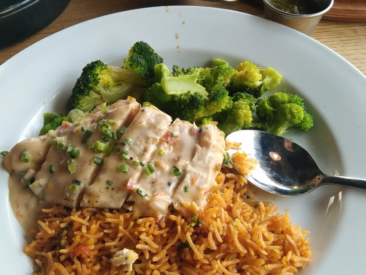 Pechuga de pollo en salsa con arroz salteado y brócoli en un plato blanco