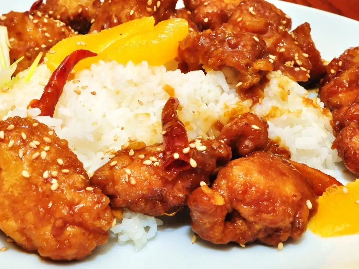Pollo rebozado en salsa de naranja con sésamo, gajos de naranja y arroz blanco