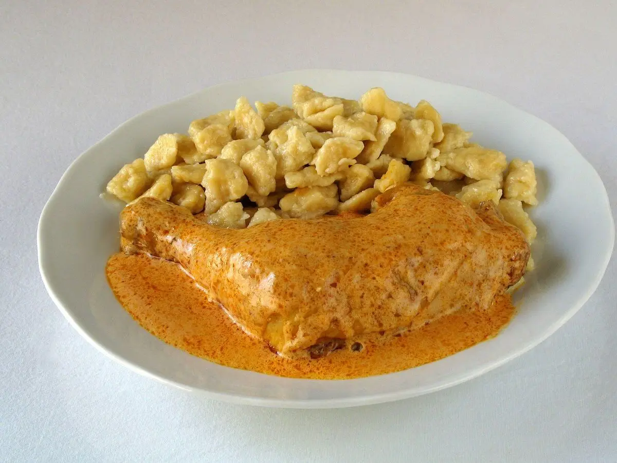 Plato blanco con pollo en salsa de pimentón naranja acompañado de pequeñas pastas de huevo