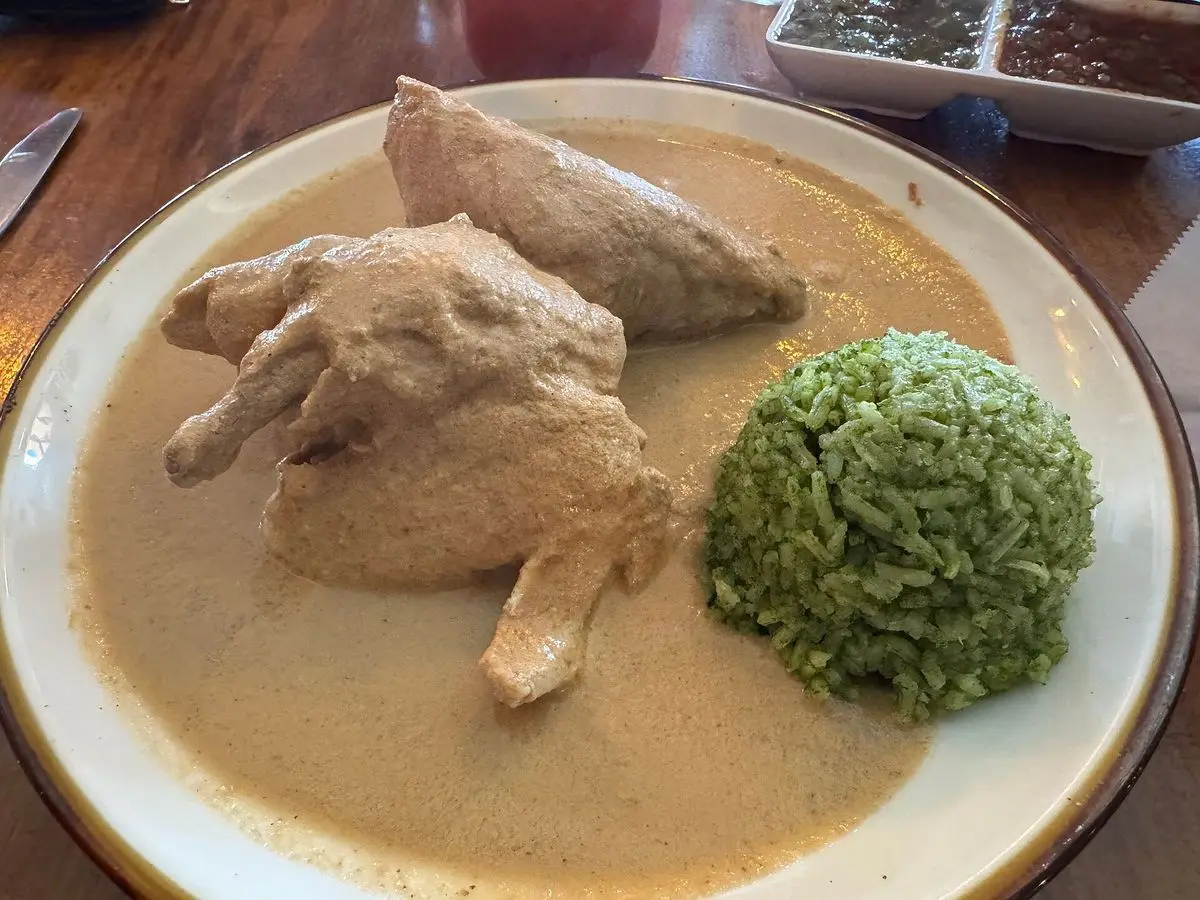 Plato con pollo en salsa cremosa de pipián y una porción de arroz verde