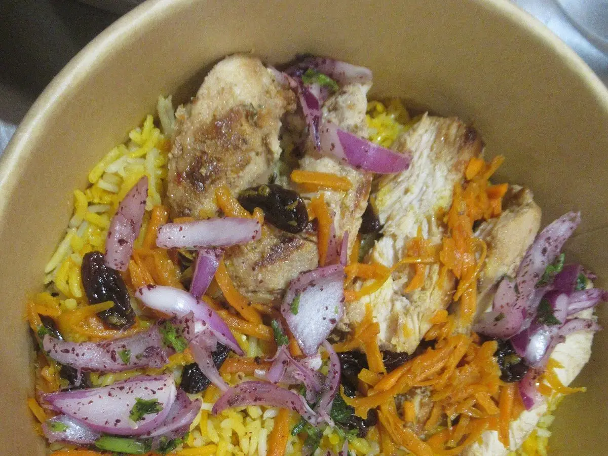 Fuente de arroz amarillo con trozos de pollo, cebolla morada y zanahoria por encima