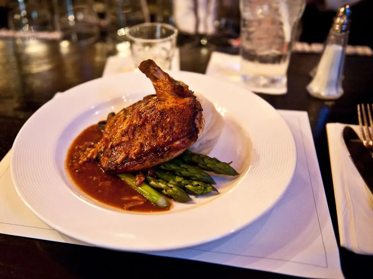 Muslo de pollo a la plancha con salsa oscura y espárragos verdes en un plato blanco
