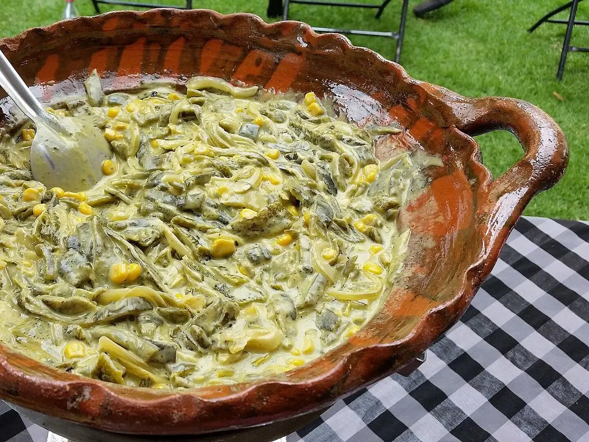 Cazuela de barro con tiras de chile poblano en salsa cremosa sobre mantel de cuadros