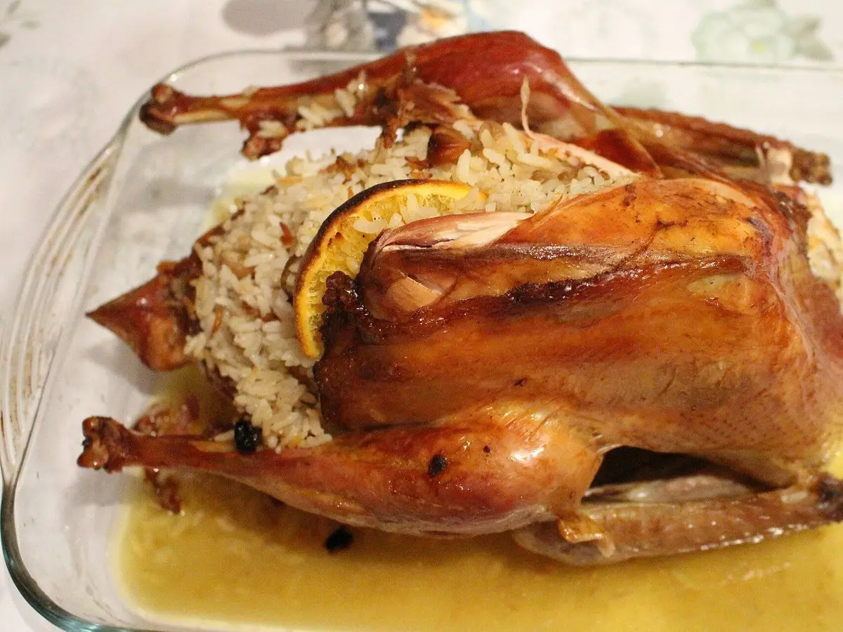 Pollo entero asado relleno de arroz, con rodajas de naranja, en una fuente de horno