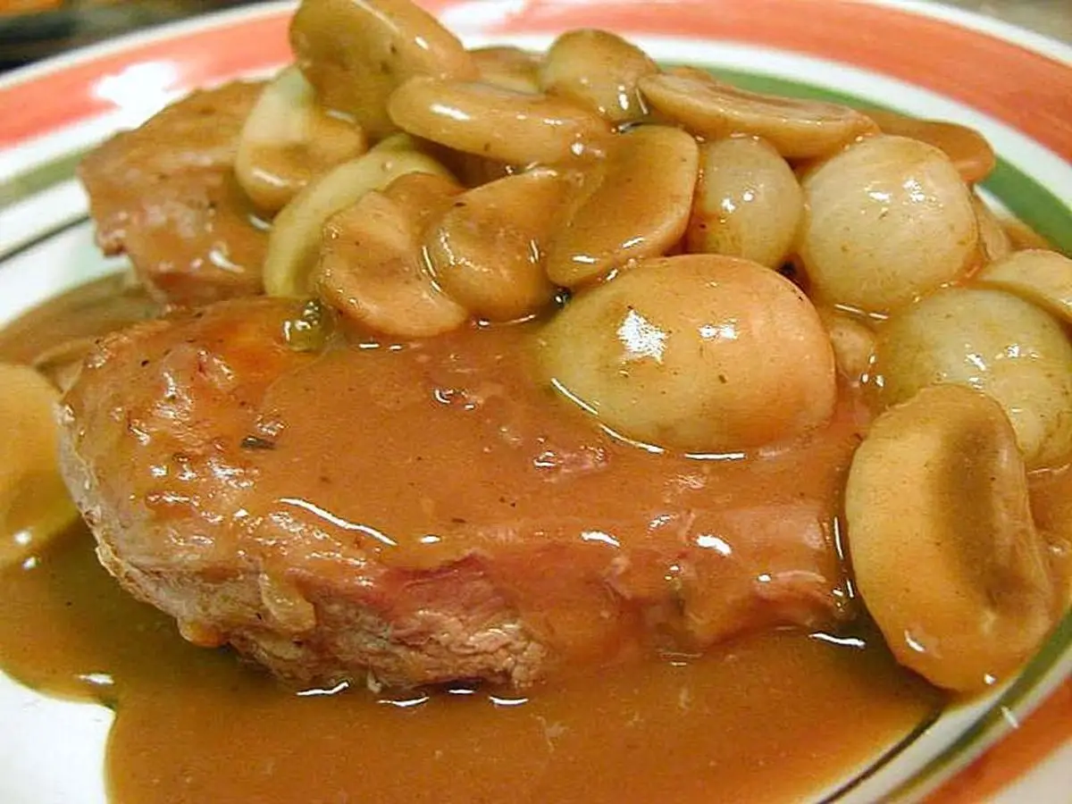 Filete de pollo en salsa con champiñones enteros sobre un plato blanco con borde de colores