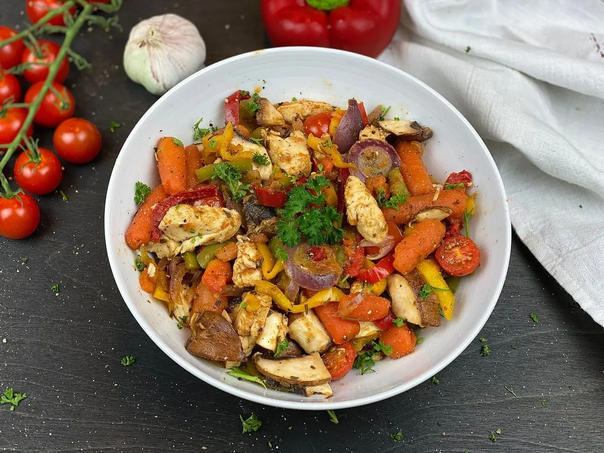 Cuenco blanco con pollo salteado, zanahoria, pimiento y cebolla morada con hierbas