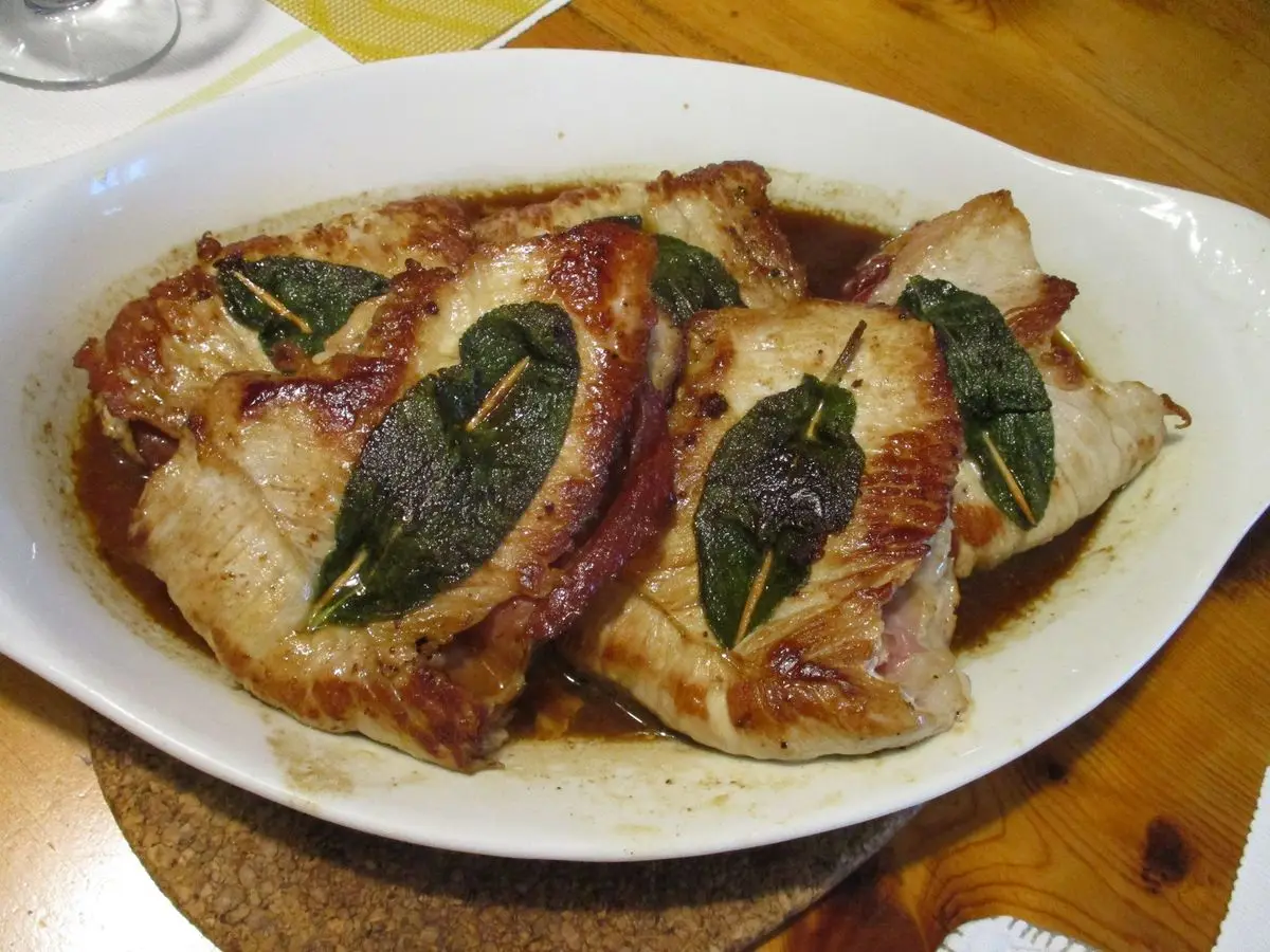 Filetes de carne dorados con hojas de salvia sobre una fuente blanca ovalada