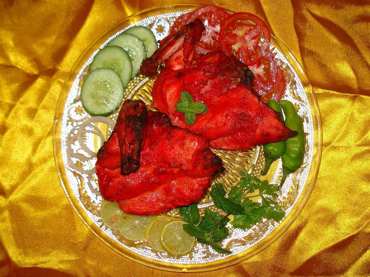 Pollo tandoori rojo con rodajas de pepino, tomate y cilantro sobre un plato dorado