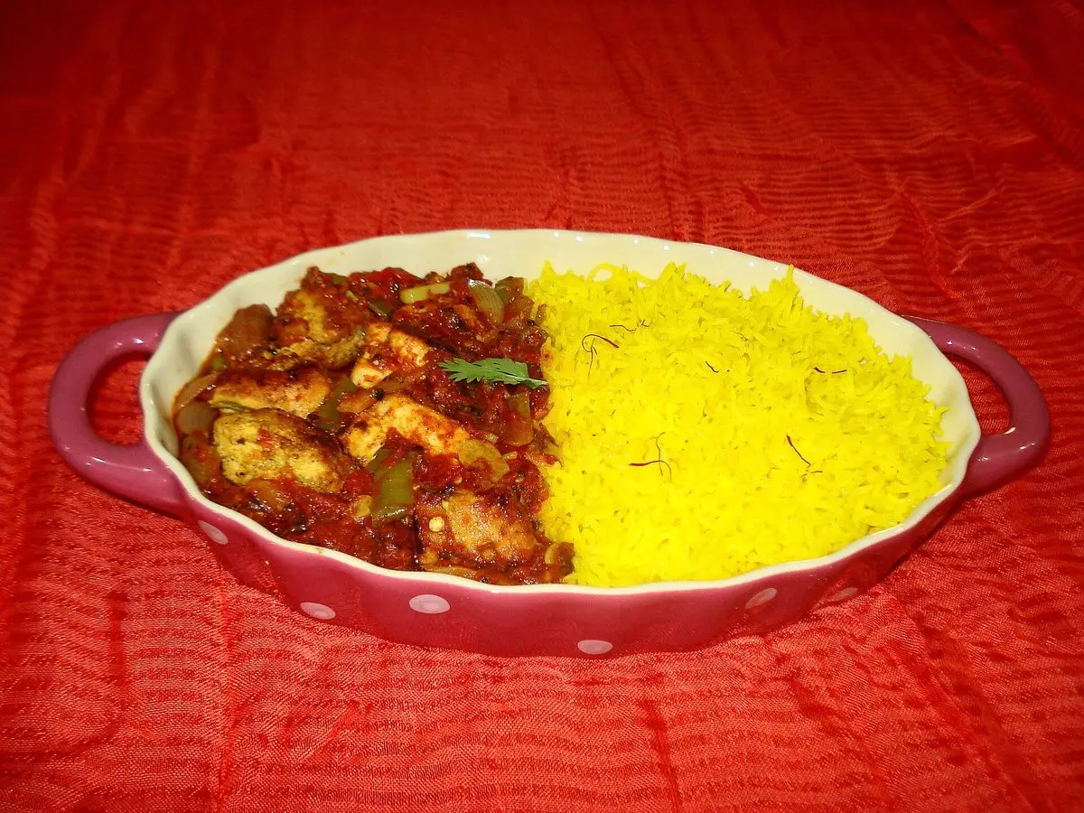 Pollo en salsa especiada de tomate junto a arroz amarillo en una fuente ovalada