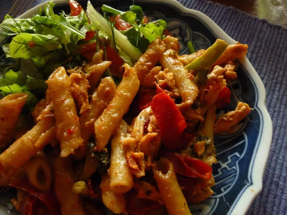 Cuenco de pasta penne con pollo y pimiento rojo, acompañado de ensalada de hojas verdes