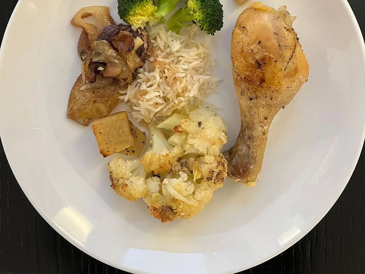 Muslo de pollo con brócoli, setas y arroz blanco servidos en un plato blanco