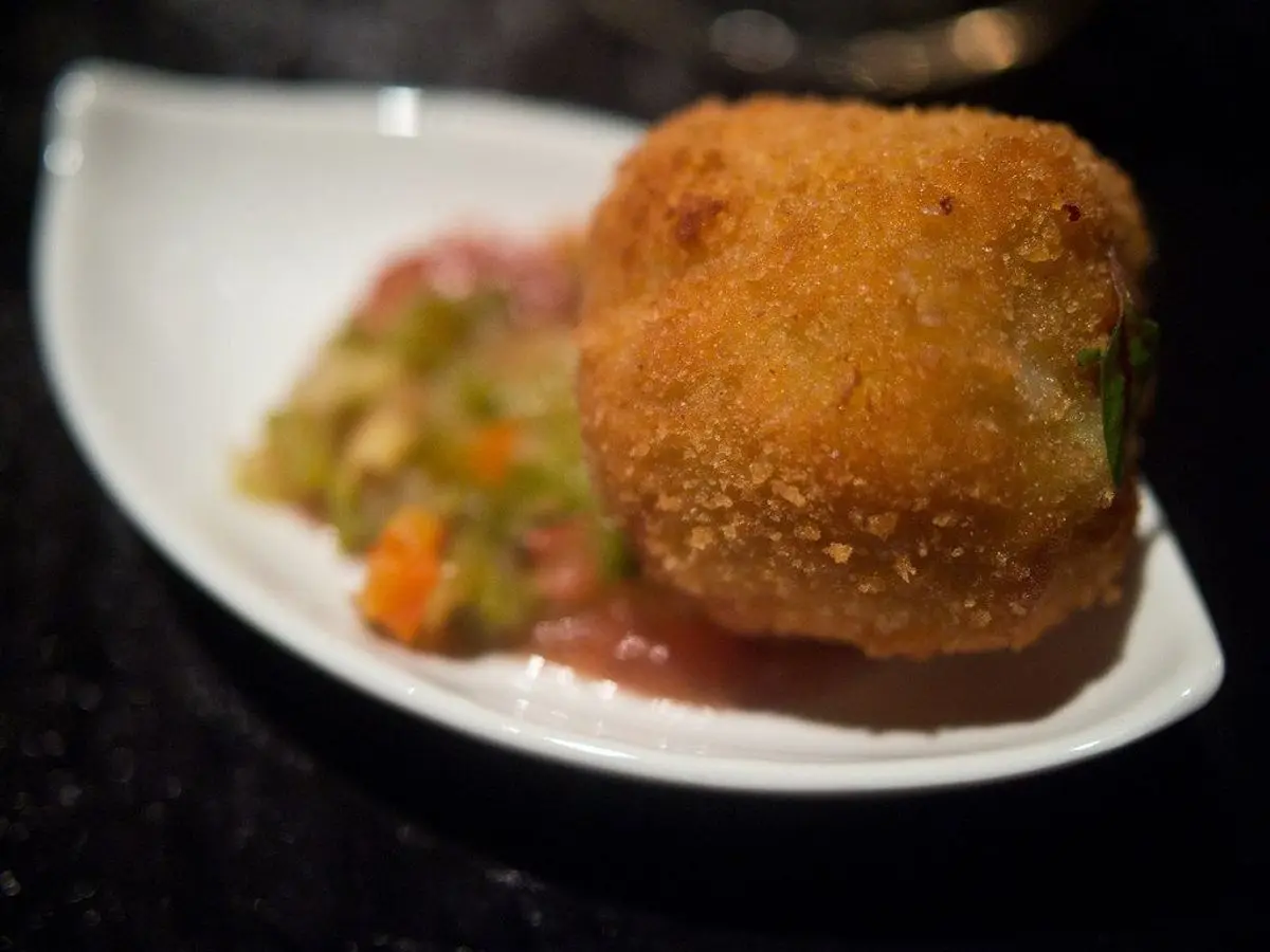 Croqueta dorada y empanada sobre un plato blanco con guarnición de verduras