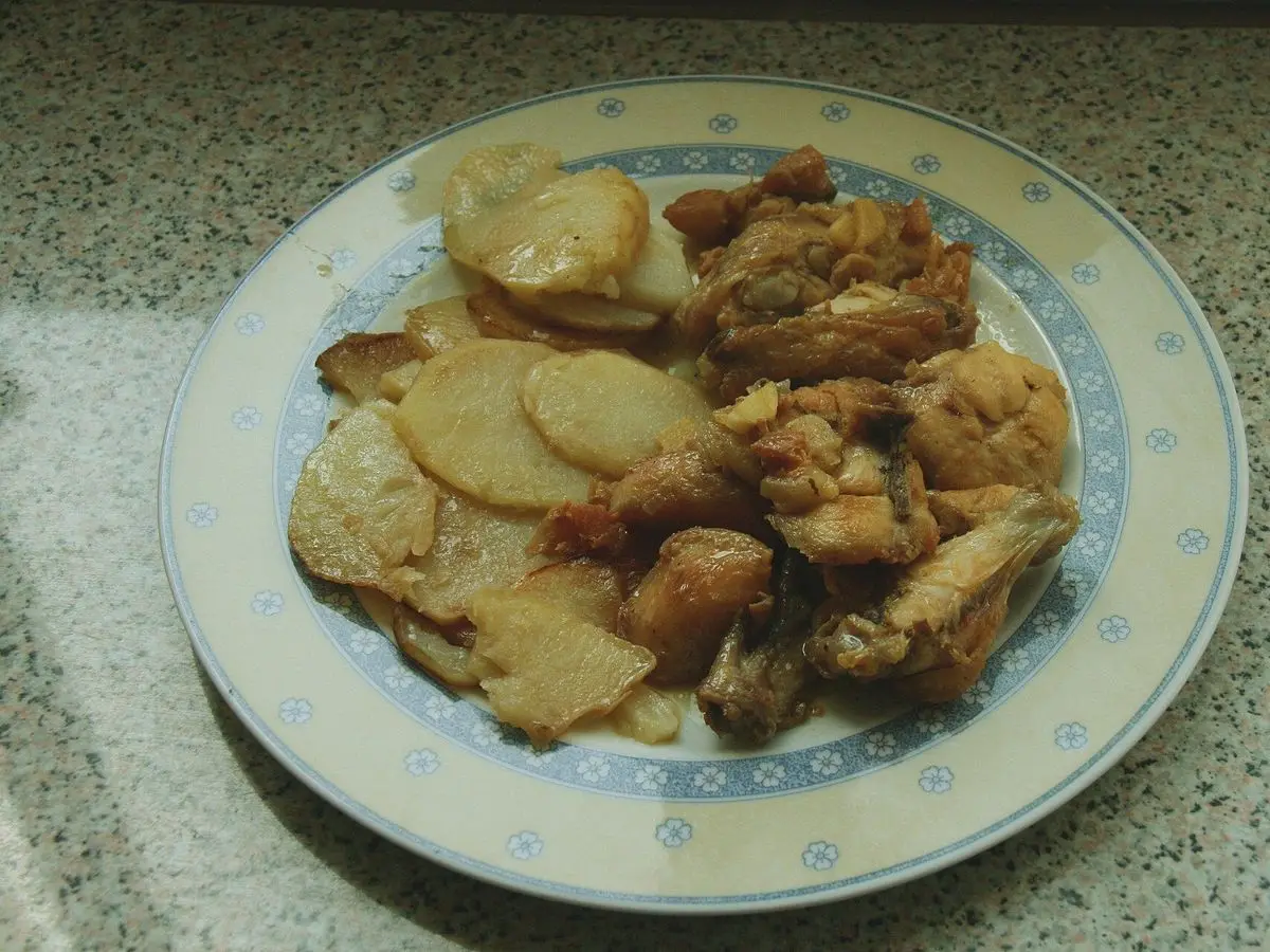 Plato con trozos de pollo guisado y rodajas de patata panadera