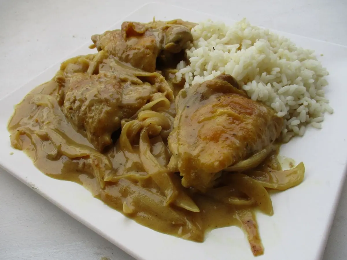 Pollo en salsa de cebolla con arroz blanco en un plato cuadrado blanco