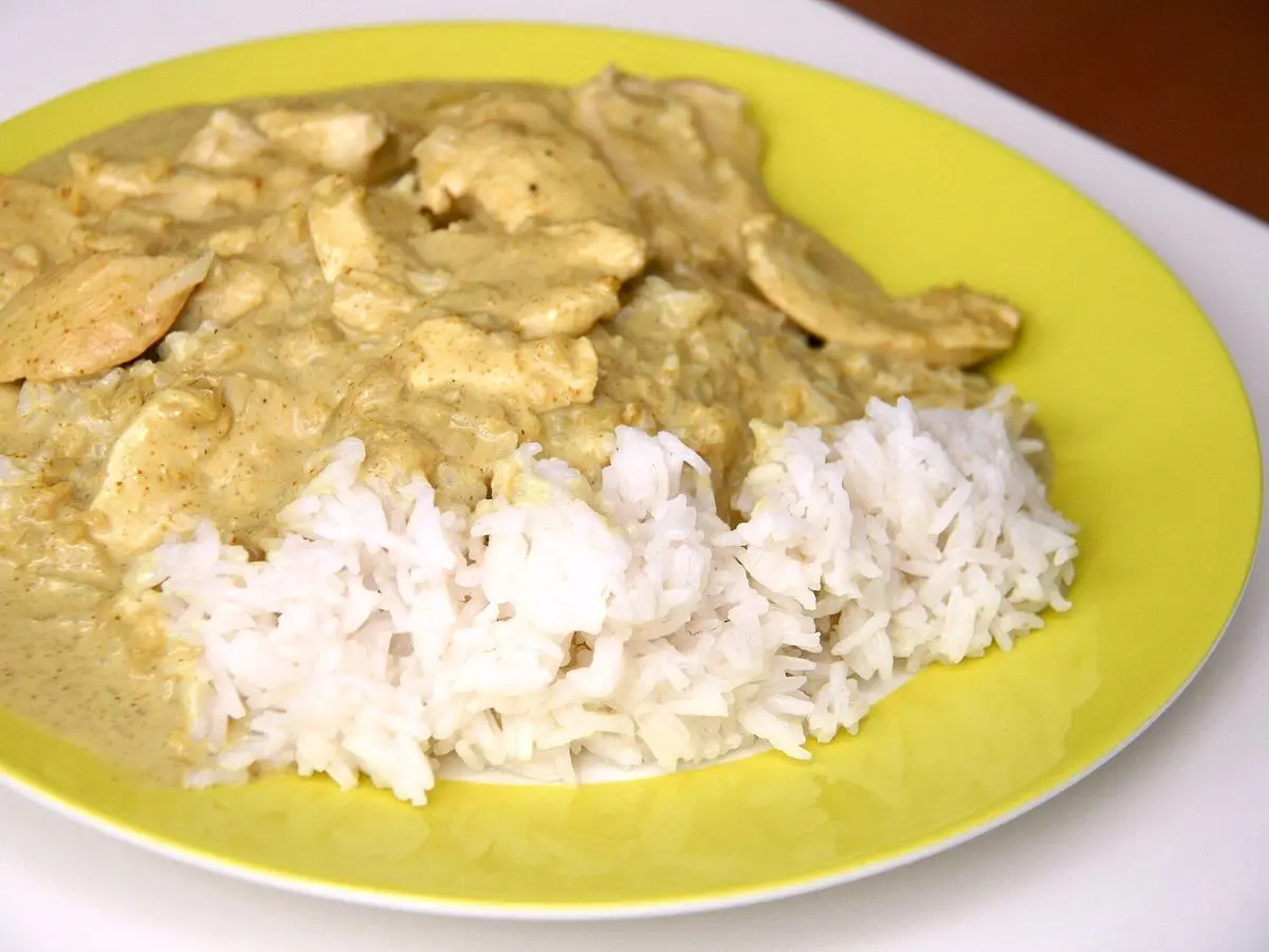 Plato amarillo con trozos de pollo en salsa cremosa de leche de coco junto a arroz blanco