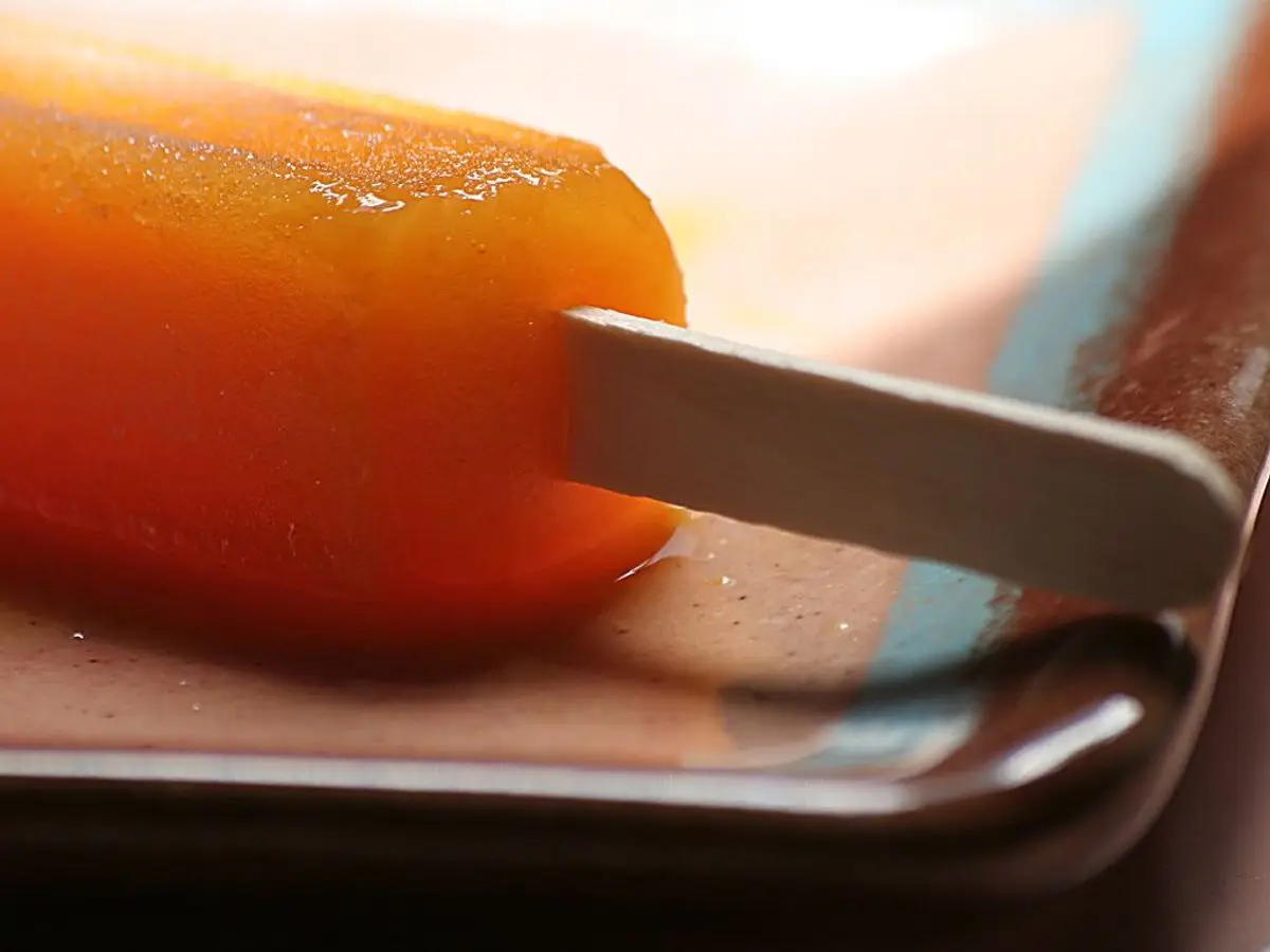 Polo casero de fruta de color naranja intenso con palo de madera, en primer plano