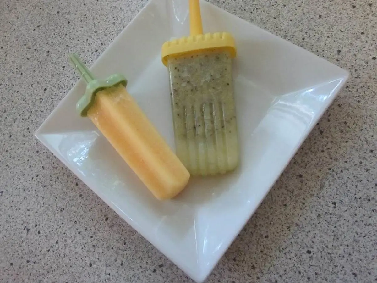 Dos polos caseros, uno amarillo anaranjado y otro de kiwi, sobre un plato cuadrado blanco