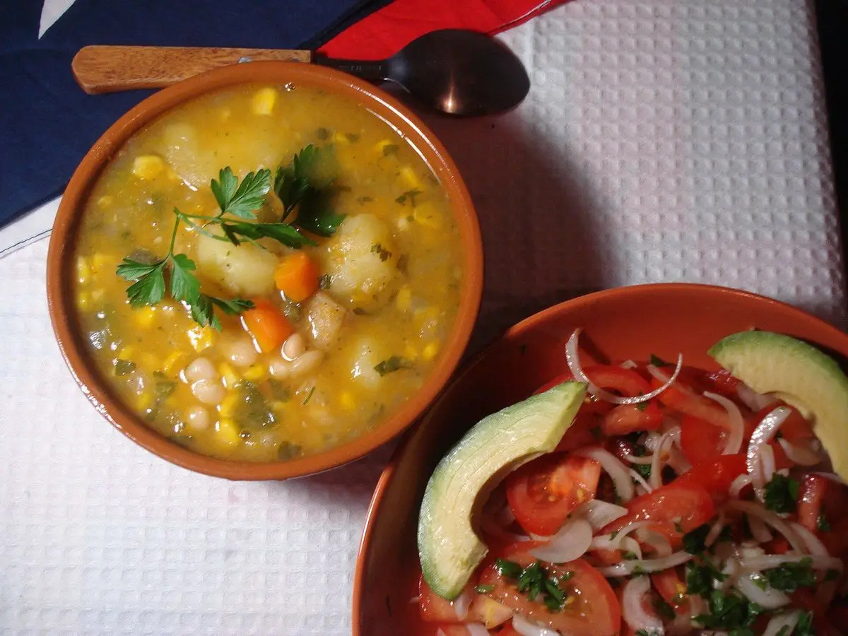 Cuenco de barro con porotos granados, calabaza y maíz junto a ensalada de tomate y aguacate