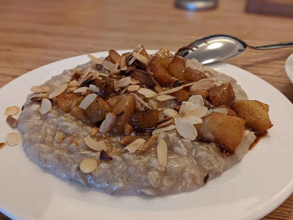 Plato blanco de avena cremosa con manzana caramelizada y láminas de almendra tostada por encima