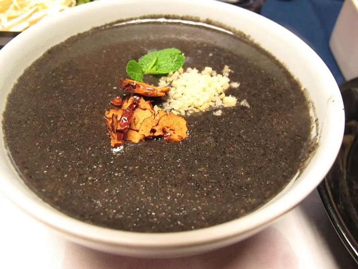Cuenco blanco de gachas de sésamo negro con una hoja de menta y frutos secos picados por encima