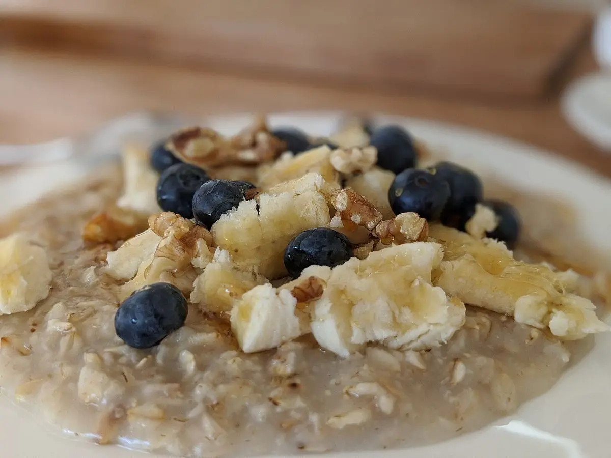 Cuenco de porridge de avena con arándanos, nueces y plátano en un plato blanco